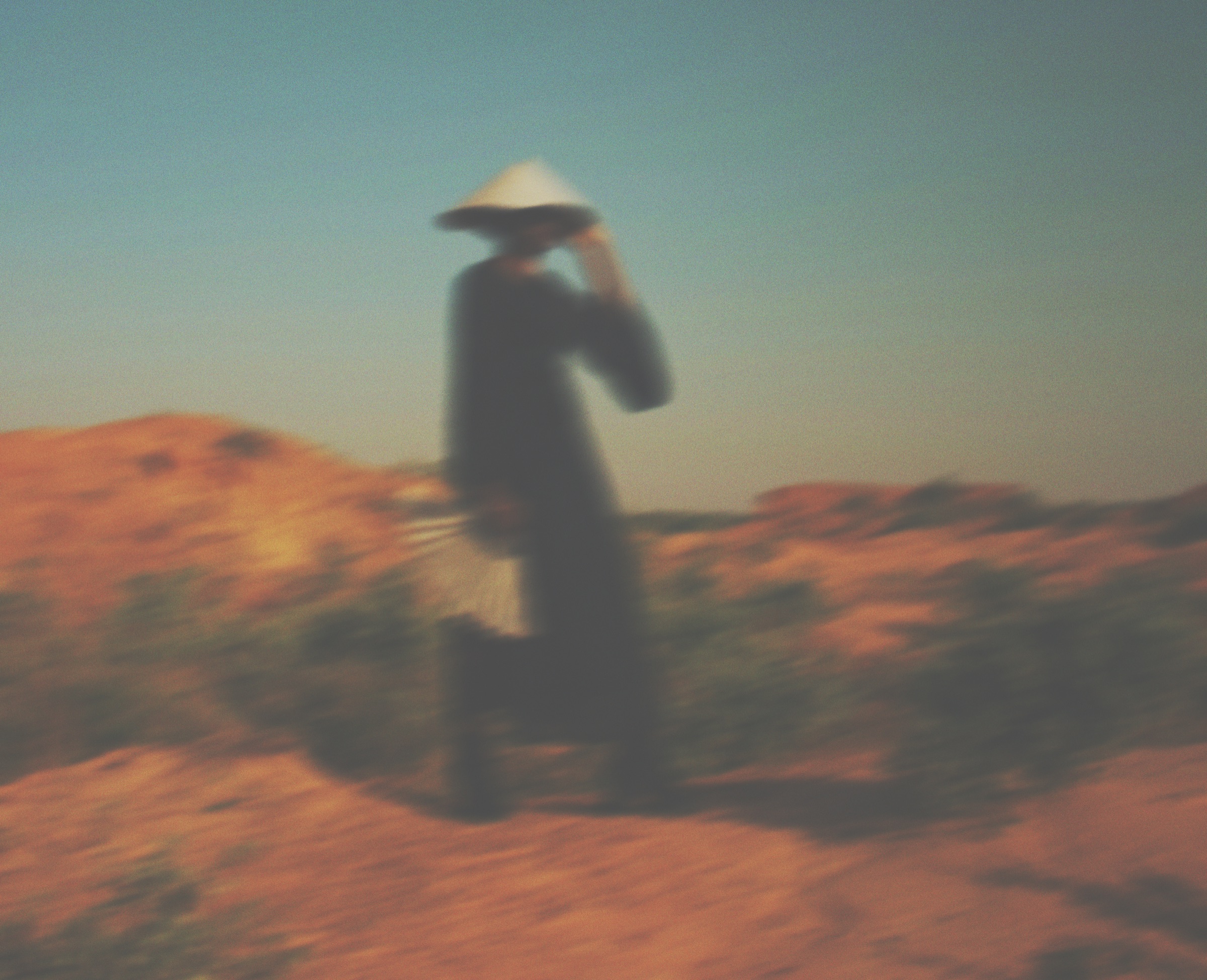 Blurred figure in a conical hat walking through dunes